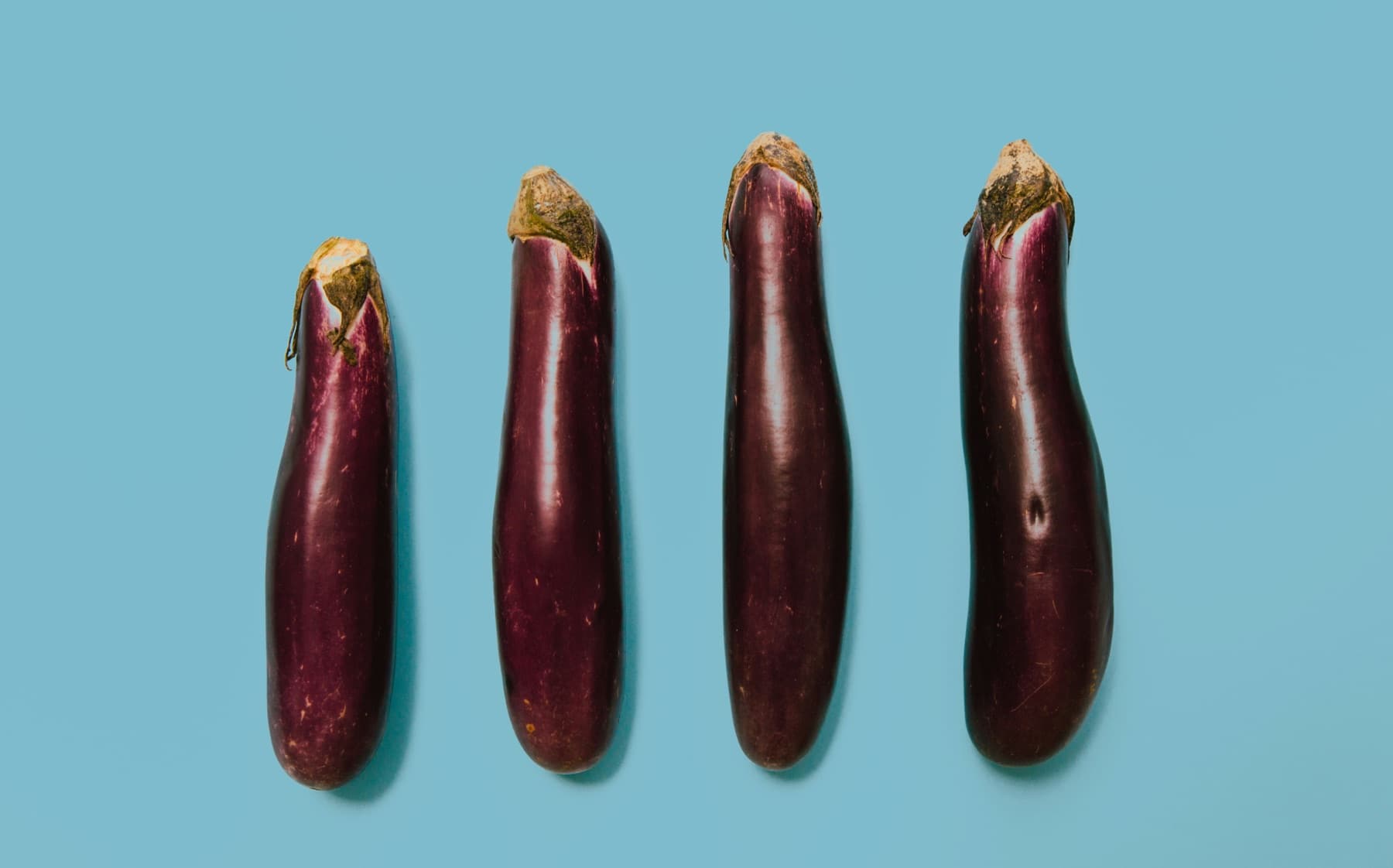 Four aubergines standing in a row on a blue background